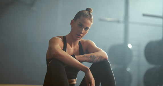 Fitness, gym and portrait of a woman on a break while training for wellness, health and strength. Healthy, strong and young athlete sitting on the floor to rest during a workout at a sports studio.