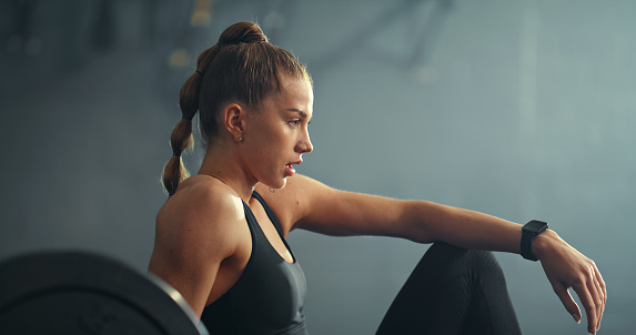 Fitness, motivation and woman tired from weightlifting, training and doing a cardio workout in the gym. Thinking, young and strong athlete breathing and relax with fatigue after exercise at a club