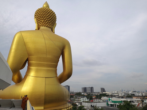 Monks standing at the 69 mt tall golden big Buddha at Wat Paknam Bhasicharoen, a royal Wat in Phasi Charoen district, Thailand.