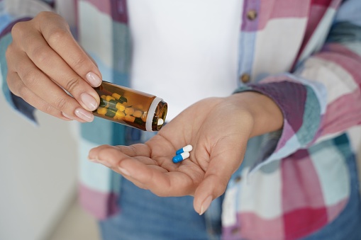 Female pour pills into palm, taking medicine, vitamins, painkiller or dietary supplement. Close up of woman's hands with medication capsules and medical jar. Health care, treatment, cure concept.