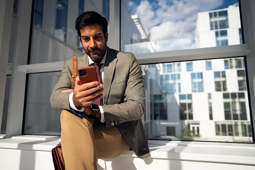 Businessman using his phone while sitting in the hall of a corporate building.