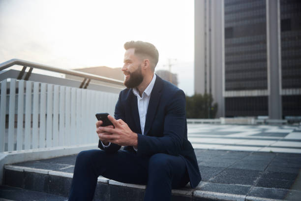 istock Smiling businessman using his phone while sitting outside an office building 1436981198