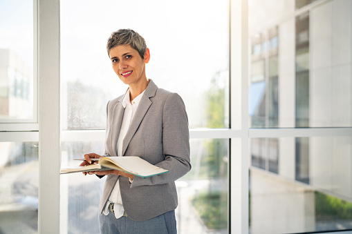 Positive young woman manager sitting at desk and looking back at camera during meeting with colleagues in conference room in company office.