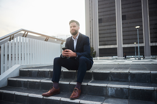 Young businessman smiling while texting on his smart phone on steps outside of an office building