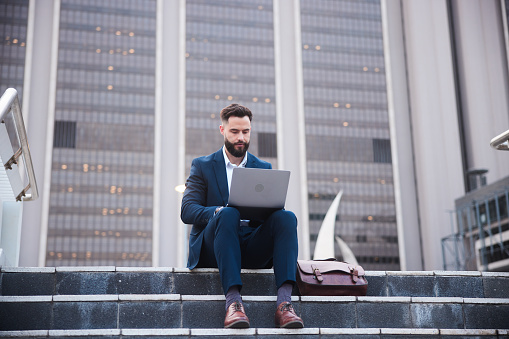 Young businessman working on a laptop while sitting on steps outside of an office building