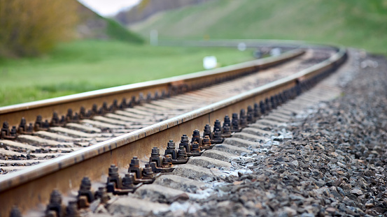 Selective focus railway track turns and twists between hills. Empty rounding and turning single track of railways. Shallow focus perspective view of rounded rails bend horizontal, 16x9.