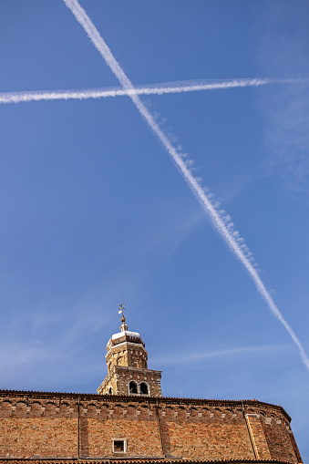 Murano, Venice, Italy - October 8th 2022: Two crossing vapor trails over the San Pietro Martire church on Murano, a small island which is a kind of suburb to Vencie