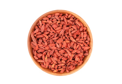 Dried goji berries, or wolfberry, in a round terracotta bowl on white background. Top view.