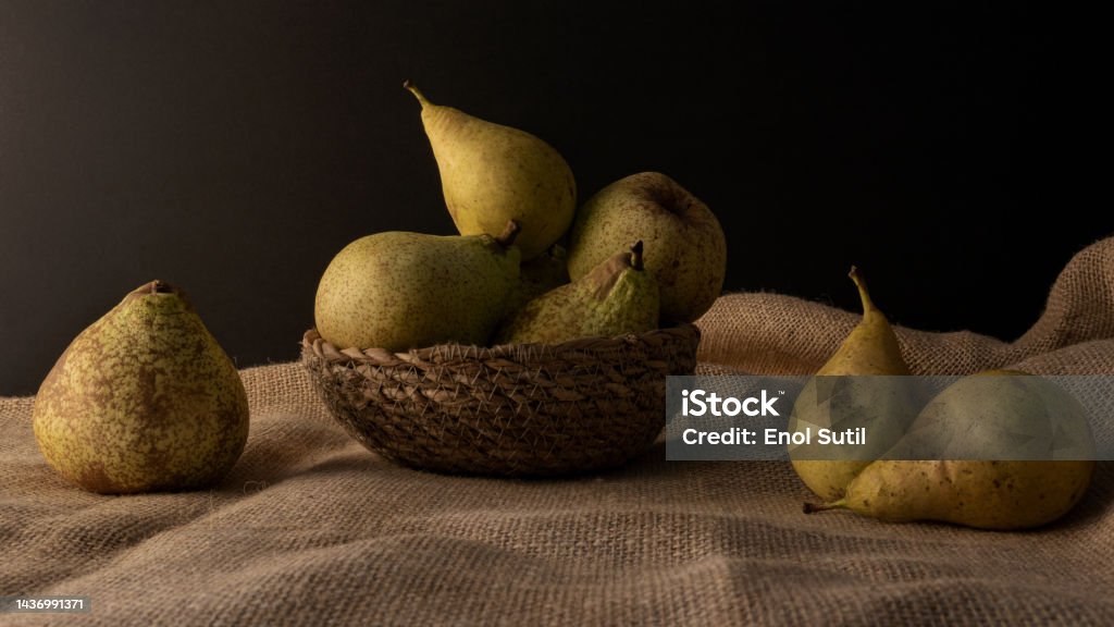 Close up of a freshly picked pears  over a jute surface on dark backdrop Fruit in a basket with scattered pears around in black background over a jute surface Abundance Stock Photo