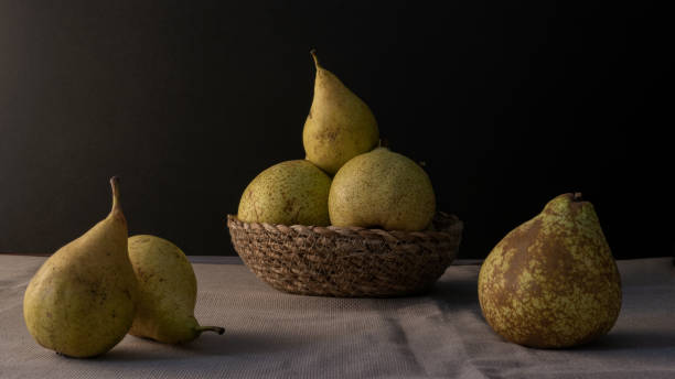 Three pears in a rattan basket with black background Green pears in a little rattan basket with more pears near them with a black background forelle pear stock pictures, royalty-free photos & images