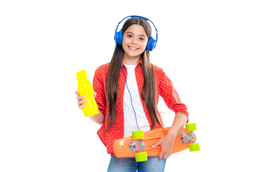 Teen hipster girl skater with skateboard water bottle and headphones on white isolated background. Summer kids trend, urban teenage style. Portrait of happy smiling teenage child girl