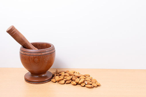 Dark wood mortar and almonds, on a wooden base and white background