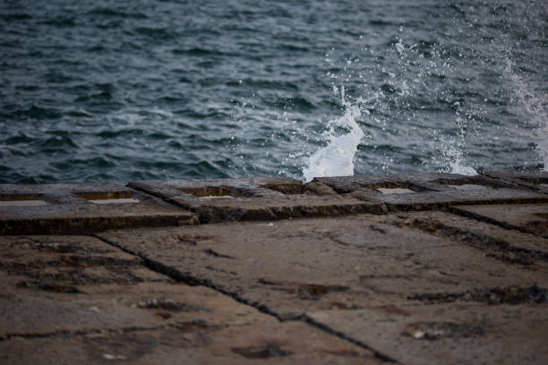 A sea wave hits the pier from stone slabs, water splashes flying to the sides. Nobody is on the waterfront. Seascape with storm surge and sea spray. Black Sea, Odessa, Ukraine.