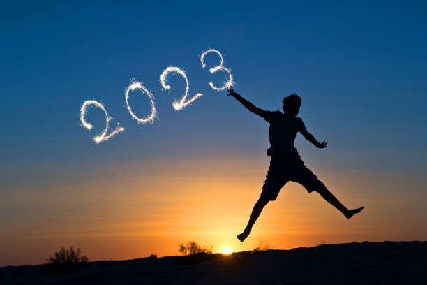 2023 written with sparkles, silhouette of a boy jumping in the sun, new year card stock photo