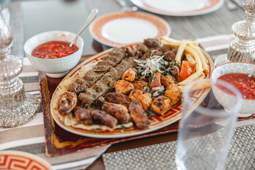 On brown dining table there is traditional middle eastern main dish and red sauces on the side. In the background there are plates.