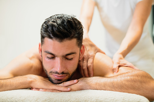 Handsome bearded male client of massage salon lying on table and getting back massage on resort spa