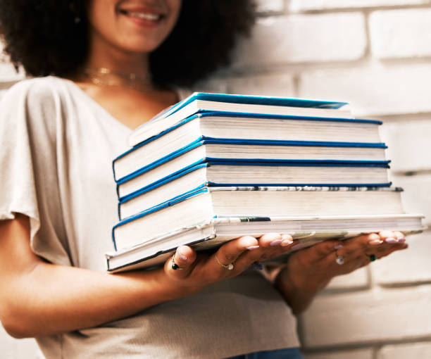 estudiante de educación, conocimiento y aprendizaje con libros para estudiar, investigar o realizar tareas en una pared blanca. beca negra, geek o chica nerd con pila de libros de texto de la biblioteca universitaria para leer - nerd student female exam fotografías e imágenes de stock