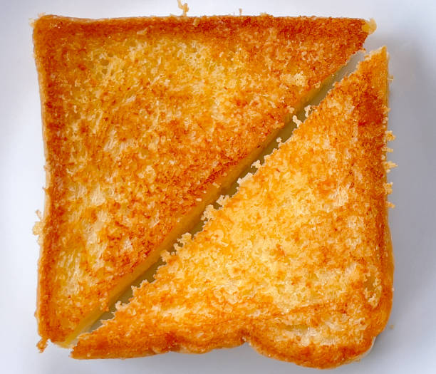 Two piece triangle slices of toasted bread made from white wheat flour and a slice of cheddar cheese in white plate.