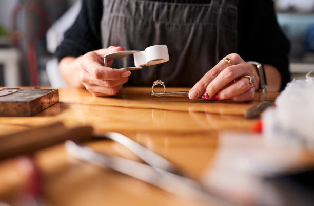 Jewelry, diamond ring and magnifying glass in creative workshop, luxury product studio and manufacturing. Hands of woman jewellery designer inspection, check and production tools for quality control