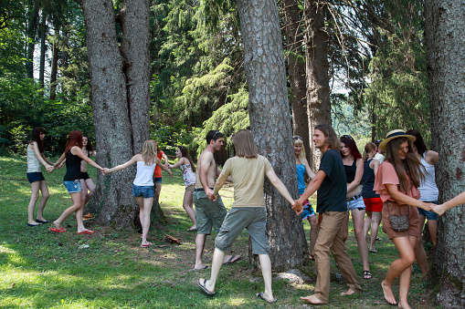 Young people dancing around and hugging trees. Large group of young people in forest.