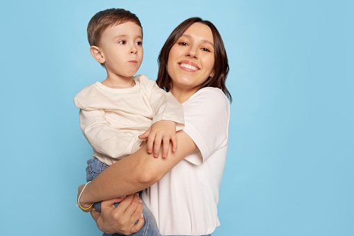 happy young woman and little boy, mother hugging her son isolated on blue studio background. Mother's Day celebration. Concept of family, childhood, motherhood, sincere emotions