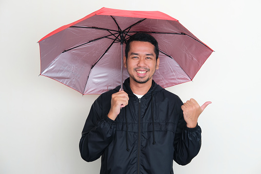 Adult Asian man wearing jacket and using an umbrella with happy expression