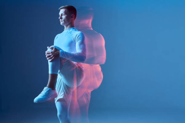 istock Strong man in white sportswear on blu background in studio stretches his leg. Athlete getting ready for run, workout, exercise. 1437011912