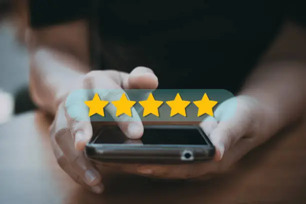 Photo of review rating and feedback 5 stars, the best and excellent admire by reviewer, close up on customer hand pressing on smartphone screen with gold five star
