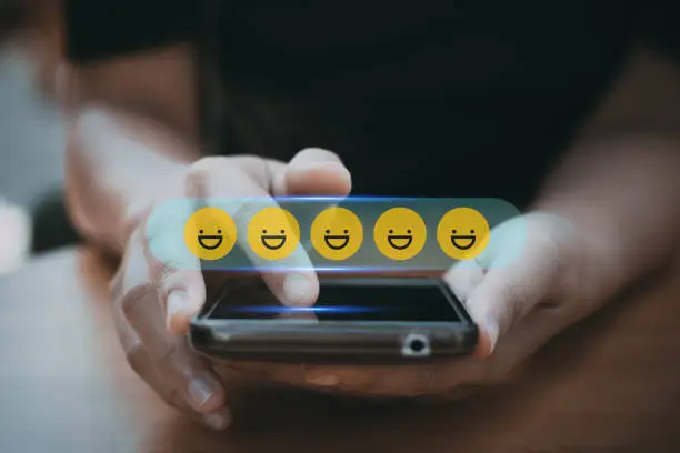 Photo of review rating and feedback, the best and excellent admire by reviewer, close up on customer hand pressing on smartphone screen with gold emoji faces