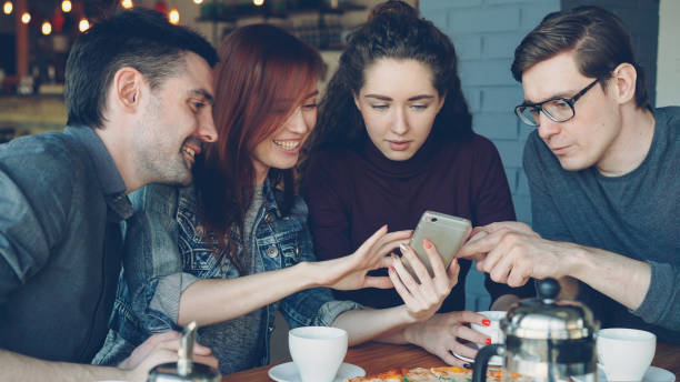 istock Cheerful young men and women close friends are using smartphone and talking while having lunch in nice cafe. Dining, modern technology and friendship concept. 1437030910