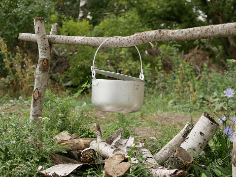 Cooking over a campfire in field conditions. A metal pot with a lid hangs over birch firewood at the place where the fire is kindled.