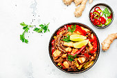Asian cuisine, stir fry noodles with chicken and vegetables, paprika, zucchini and sesame seeds in bowl. White kitchen table background, top view, space for text