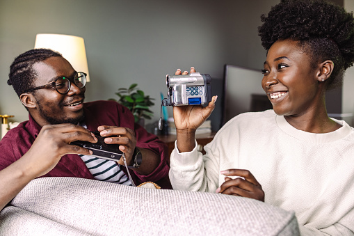 African-American young couple sitting on the sofa at home, they are playing with vintage and analog technology.
