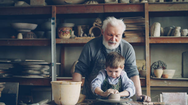 istock Elderly man experienced potter is teaching little boy how to work with clay on potter's wheel. Sharing experience, family tradition and modern pottery concept. 1437040307