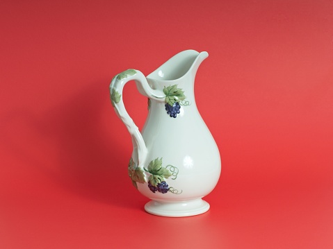 Fancy ceramic water pitcher with purple grape pattern centered on a red background.