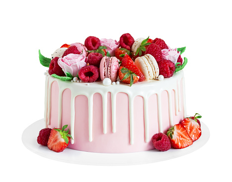 Birthday sweet cake with berries, macaron and floral decor isolated on a white background. Beautiful pink cake decorated with macarons, raspberries, strawberries and sugar rose flowers.