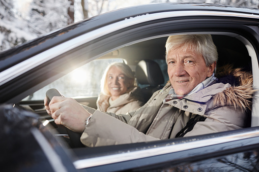 Portrait of cheerful senior couple driving car in winter, focus on senior man behind wheel looking at camera, copy space