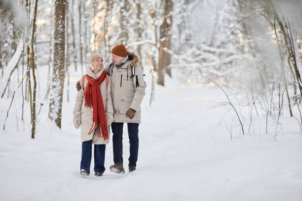 Loving Couple Walking in Winter Forest Full length portrait of happy senior couple enjoying walk in winter forest and looking at each other, copy space snow hiking stock pictures, royalty-free photos & images