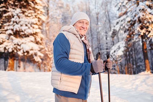Waist up portrait of smiling mature man enjoying Nordic walk in winter forest at sunset, copy space