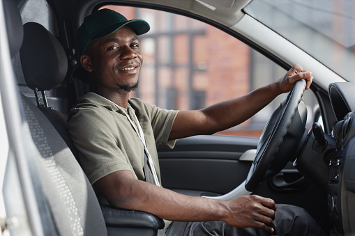 Side view portrait of smiling delivery man driving truck and looking at camera
