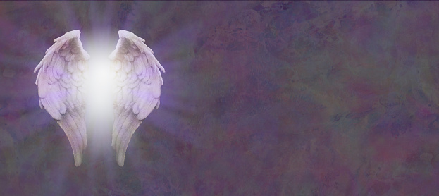 Pair of angel wings in a white light burst against a stone textured dark background with copy space on right side