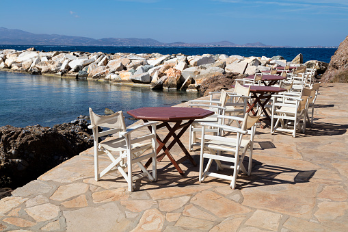 Tables and chairs near Mediterranean Sea, outdoor restaurant in Naxos, Greece.