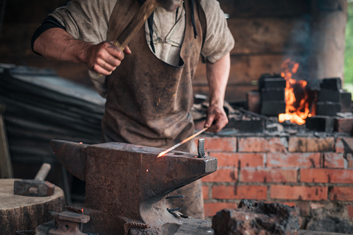 Hands of a man with a hammer on the background of an authentic retro forge with bright fire.