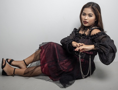 A Filipina in a vampire costume touching her hand while sat on white background