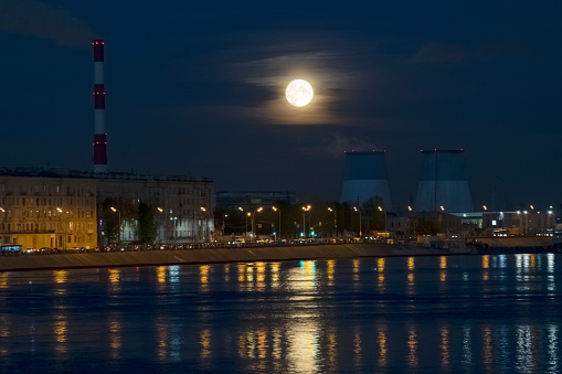 the rising moon in the clouds over two cooling towers, reflected in the surface of the river