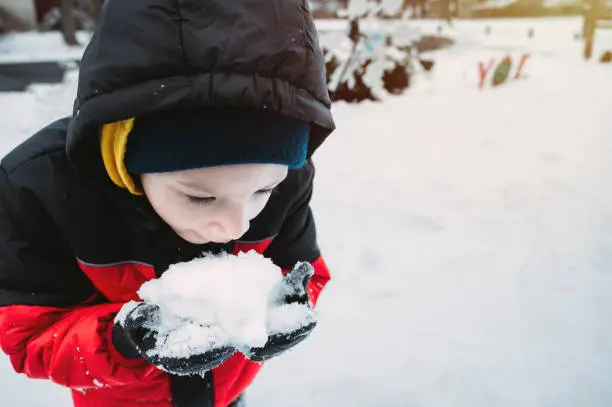 Boy eating and plying with snow and has fun. Outdoor activities for Christmas vacation.