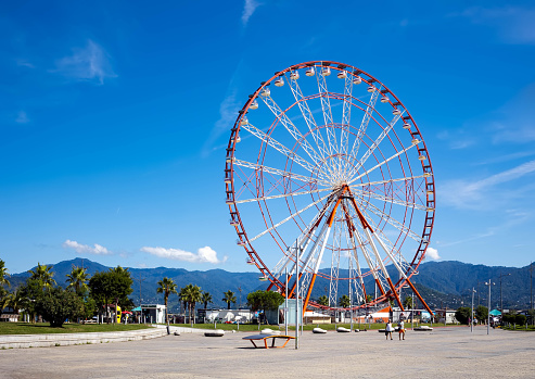 Batumi, Georgia - September 15, 2022: Ferris wheel Mountain view on a sunny summer day against a bright blue sky.