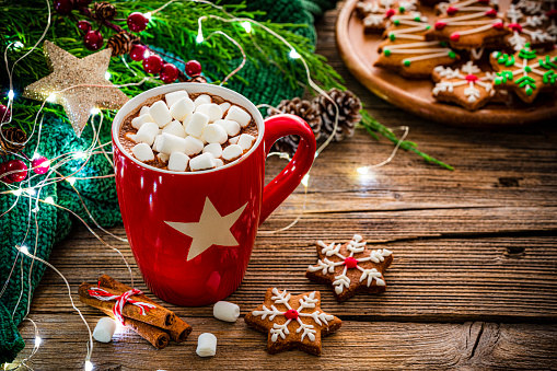 Close up view of a hot chocolate mug with marshmallows shot on rustic wooden Christmas table. Homemade Christmas cookies and Christmas decoration complete the composition. The composition is at the left of an horizontal frame leaving useful copy space for text and/or logo at the right. High resolution 42Mp studio digital capture taken with Sony A7rII and Sony FE 90mm f2.8 macro G OSS lens