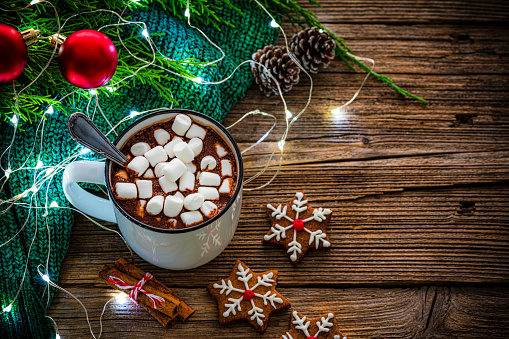 High angle view of a hot chocolate mug with marshmallows shot on rustic wooden Christmas table. Homemade Christmas cookies and Christmas decoration complete the composition. The composition is at the left of an horizontal frame leaving useful copy space for text and/or logo at the right. High resolution 42Mp studio digital capture taken with Sony A7rII and Sony FE 90mm f2.8 macro G OSS lens