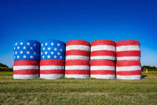 A flag of the United States of America on hay bales in a country scene.